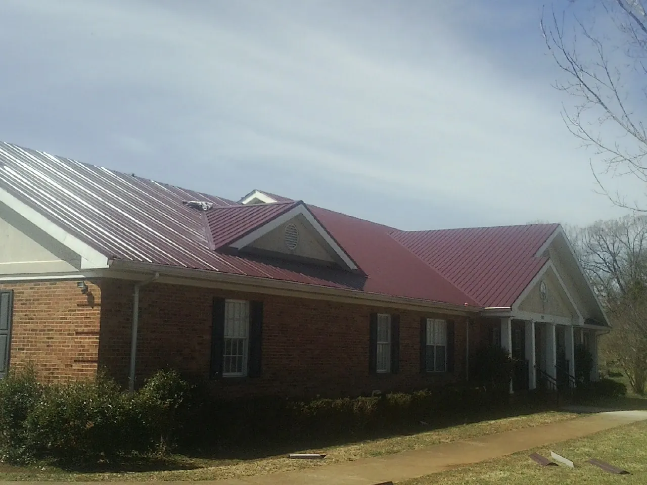 Red metal roof with gabled entries on a long brick building, from a Hail Damage Roof Repair job in Wakarusa