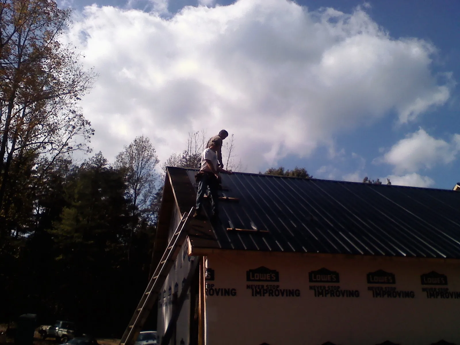 Roofer fastening dark metal panels high against a cloudy sky, from a Roof Inspection job in Wakarusa