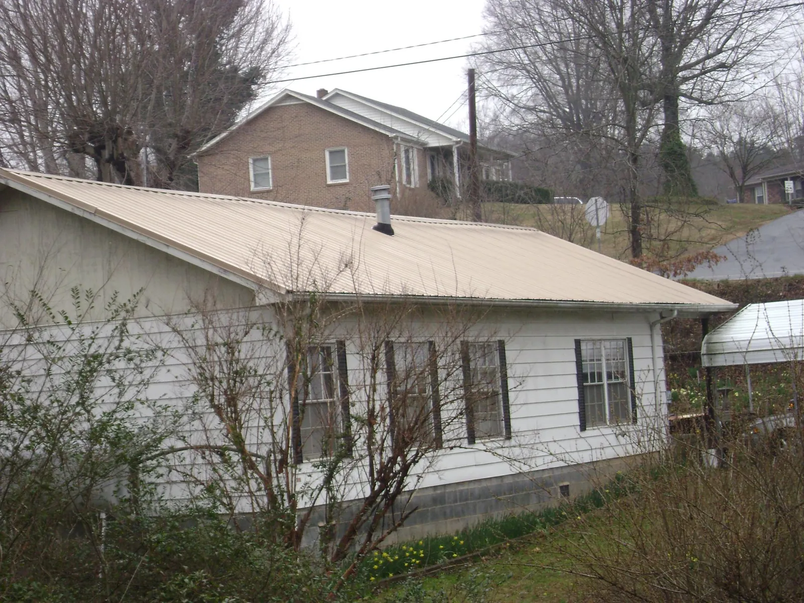 Tan metal roof on a white sided house set into a hillside — Commercial Roofing by Roofing Brothers in Wakarusa