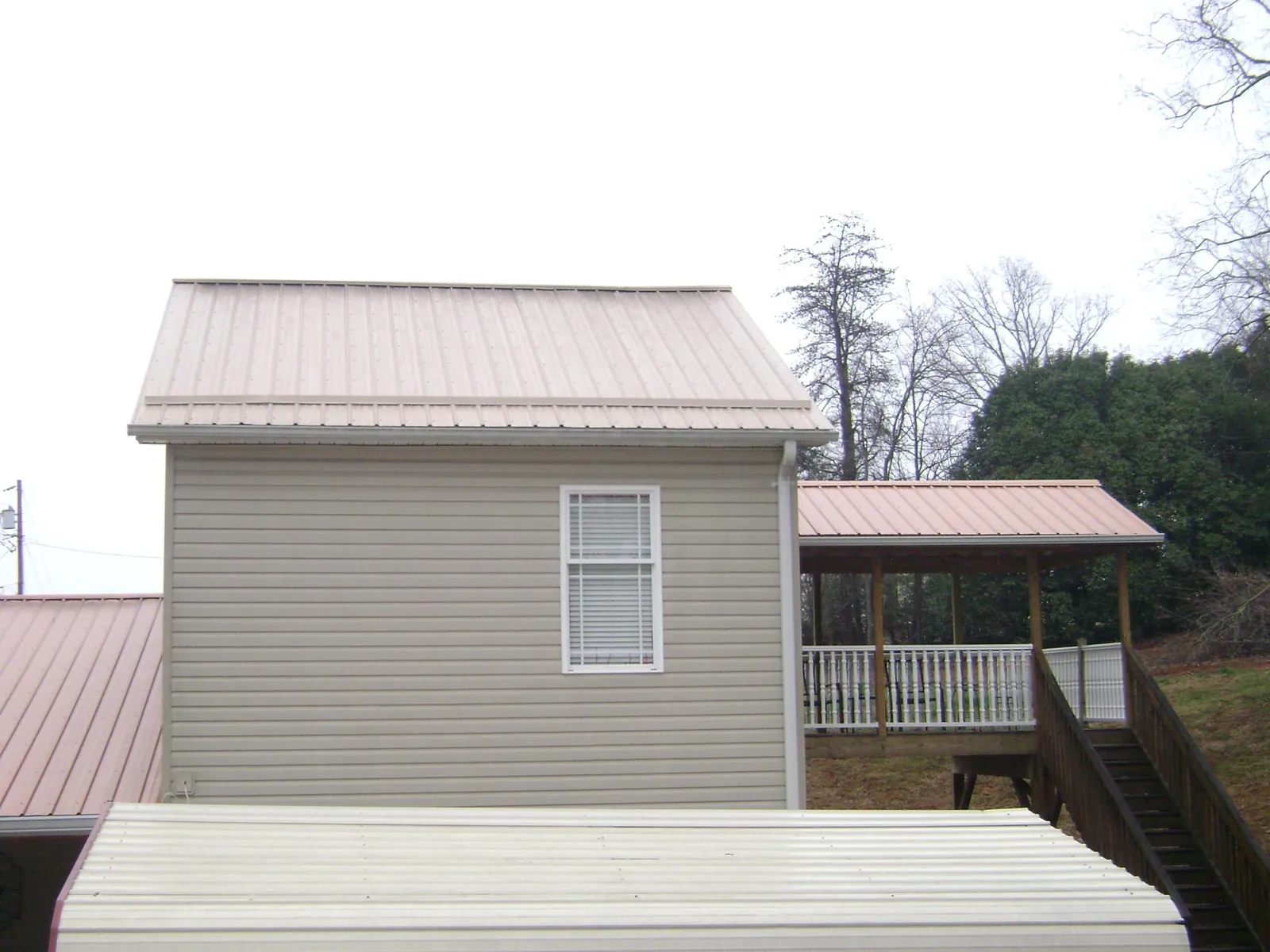 Tan metal roofs on a two story addition and attached porch, from a Roof Replacement job in Wakarusa
